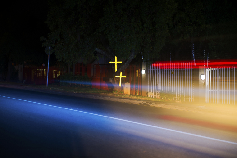 Two crosses lit up by car lights on a dark road